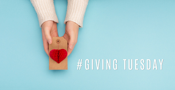 Giving Tuesday, global day of charitable giving after Black Friday shopping day. Charity, give help, donations support concept with text message red paper heart in woman hands on blue background.